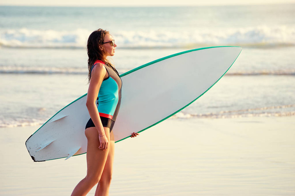 Young woman carrying surf board - Фото, изображение