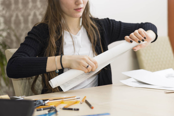 Девушка-архитектор рисует план, график, дизайн, геометрические формы карандашом на большом листе бумаги за рабочим столом
 - Фото, изображение