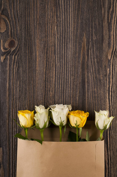 Bunch of multicolor rose flowers in paper envelope over wooden b - Foto, imagen