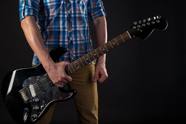 Music and art. The guitarist holds an electric guitar in his right hand, on a black isolated background. Playing guitar. Horizontal frame - 写真・画像