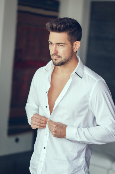 Young rich confident man buttoning shirt indoor - Photo, image