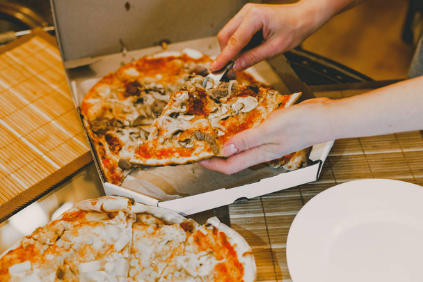 jonge vrouw de hand snijdt pizza in plakjes heerlijk warm op de tafel rustieke pizza met salami, mozzarella basilicum bovenaanzicht met kopieerruimte. Twee pizza's op een glazen tafel met tomaten en olijven - Foto, afbeelding