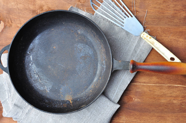 Empty black cast-iron frying pan and iron spatula on the table - Fotoğraf, Görsel