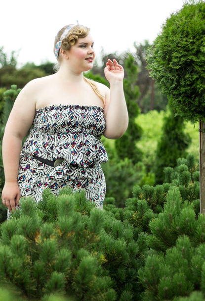 Young plus size Girl among the Evergreen plants in garden. - Fotó, kép