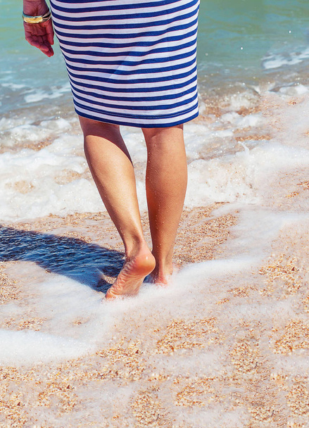 Sahilde kadın bacaklar. Denizin içinde çizgili elbiseli bir kız bacaklar. Denizin içinde kırmızı bir pedikür ile kadın bacakları. - Fotoğraf, Görsel
