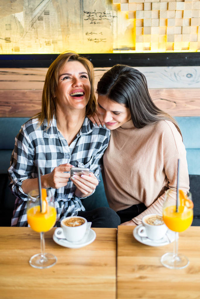 Kahvilassa istuu kaksi nuorta naisystävää, jotka juovat kahvia ja...
 - Valokuva, kuva