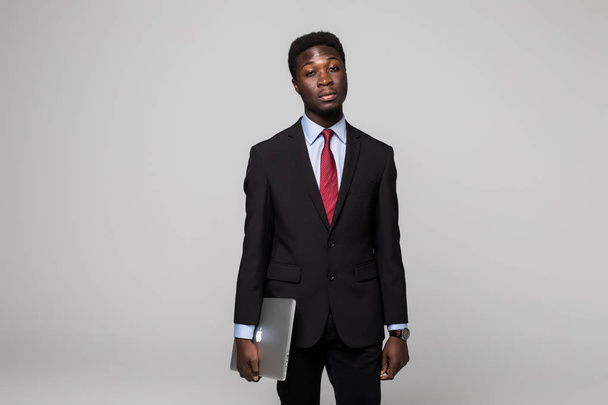 正装でハンサムな若者アフリカ灰色の背景に対して立っている間手のラップトップで移動します。 - 写真・画像