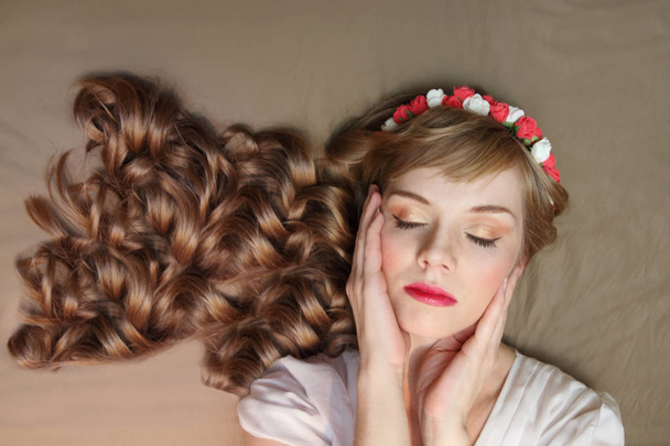 Ragazza carina in ghirlanda di rose e vestito con i capelli ricci si trova sul letto
  - Foto, immagini