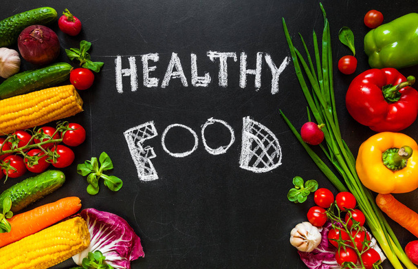 Photo of a table top full of fresh vegetables or healthy food background. Healthy food concept with fresh vegetables for cooking.Title "Healthy food"   is written by chalk on the middle of dark background. - Fotó, kép