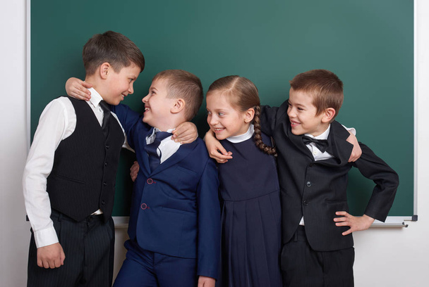 Grundschüler albern vor leerem Kreidetafelhintergrund herum, im klassisch schwarzen Anzug, Gruppenschüler, Bildungskonzept - Foto, Bild