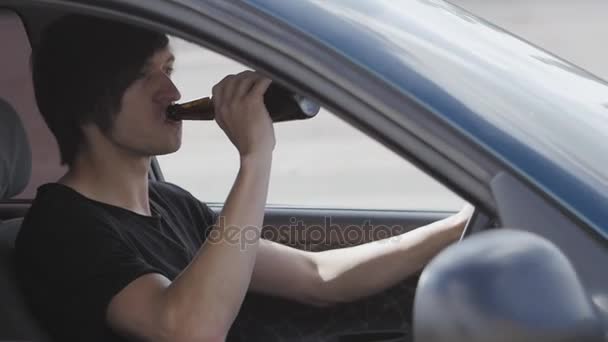 Facet pije piwo podczas jazdy samochodem. Pijany kierowca - Materiał filmowy, wideo