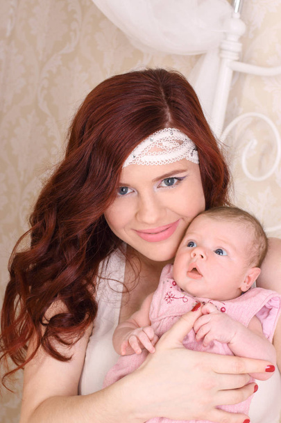 Feliz jovem mãe em um vestido de seda branca, segura seu bebê em sua
  - Foto, Imagem