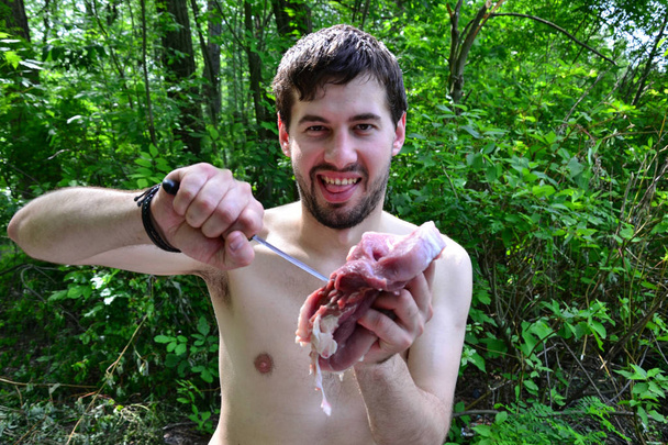 Jeune homme boucher utilisant couteau et viande crue dans les mains  - Photo, image