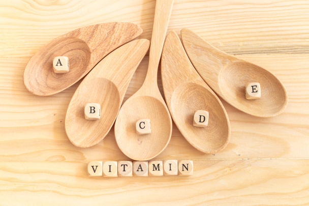 Вид сверху на витаминное слово из деревянных букв на столе и A B C D E на деревянной ложке, концепция здоровья
 - Фото, изображение