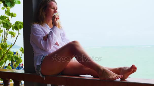 A lány ül a teraszon, és a tenger felé néz - Felvétel, videó