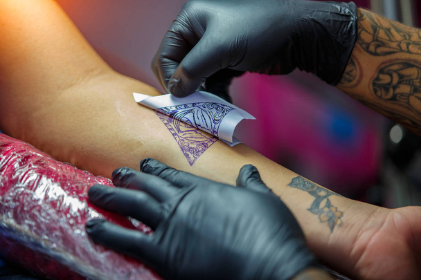 Κοντινό πλάνο τατουάζ καλλιτέχνης παρουσιάζει τη διαδικασία του να πάρει τατουάζ με χρώμα μαύρο. Κύρια έργα σε μαύρο αποστειρωμένα γάντια. - Φωτογραφία, εικόνα