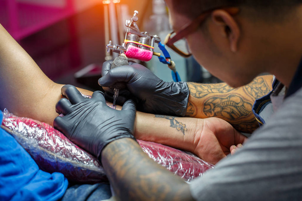 Крупним планом художник татуювання демонструє процес отримання чорного татуювання фарбою. Майстер працює в чорних стерильних рукавичках
. - Фото, зображення