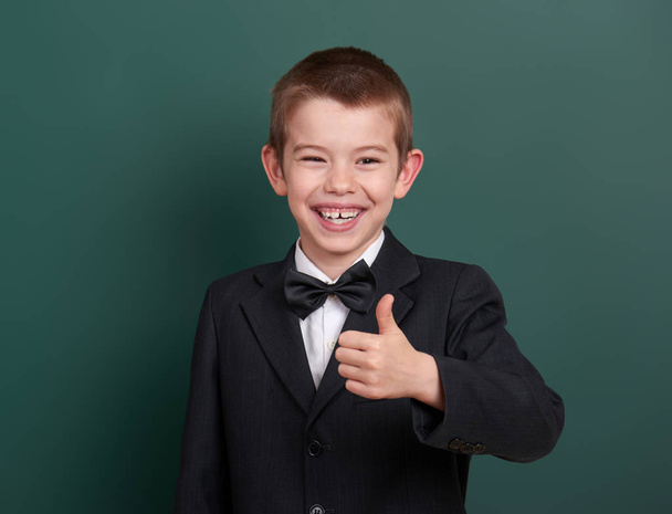 school boy show best gesture, portrait near green blank chalkboard background, dressed in classic black suit, one pupil, education concept - Foto, Imagem