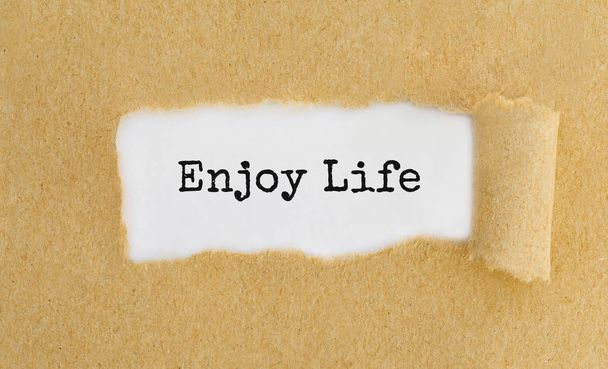 Text Enjoy Life appearing behind ripped brown paper. - Foto, Imagen