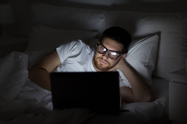 young man with laptop in bed at home bedroom - Foto, Imagen