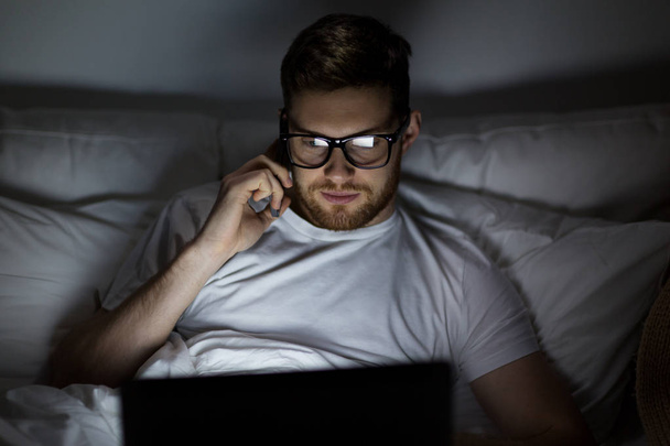man with laptop calling on smartphone at night - Photo, Image
