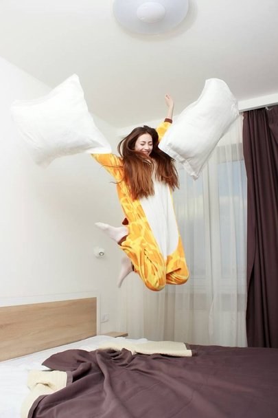 Funny girl in kigurumi pajamas jumping on the bed - Zdjęcie, obraz