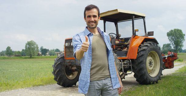 Portrait of a handsome young farmer standing in a shirt and smiling at the camera, on a tractor and nature background. Concept: bio ecology, clean environment, beautiful and healthy people, farmers. - 写真・画像