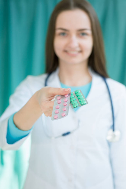 A female doctor holds out a hand with pills to the patient, photo with depth of field - Photo, Image