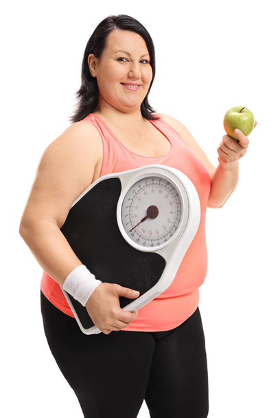 Overweight woman holding a weight scale and an apple - Φωτογραφία, εικόνα