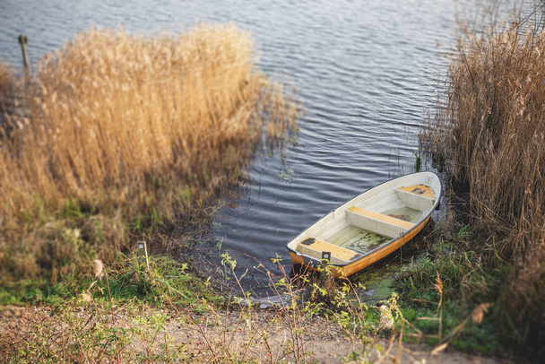 Yellow fishing boat in a dark lake in the autumn season surrounded by colorful reeds in the water - Photo, Image