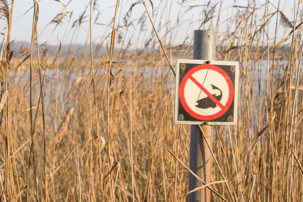 Panneau de pêche au bord d'une rivière avec de grands roseaux avec un symbole de pêche capturé avec un avertissement de non pêche
 - Photo, image