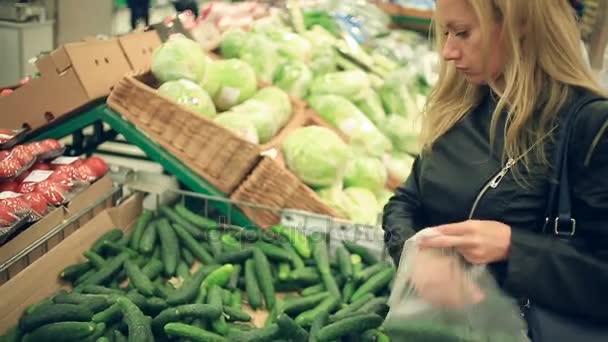 A woman in a supermarket on a vegetable shelf, buys vegetables and fruits. Man chooses cucumbers - Filmati, video