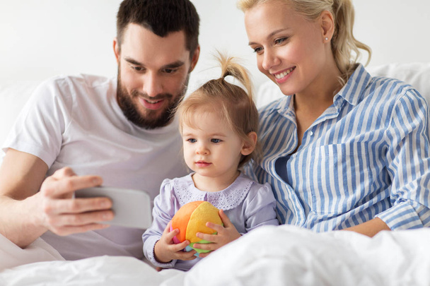 happy family with smartphone in bed at home - Фото, изображение