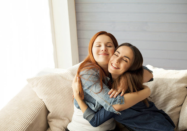 Friends hugging on sofa in living room - Фото, изображение