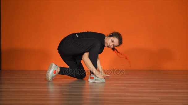 Beautiful young female break dancer against orange wall in studio - Filmati, video