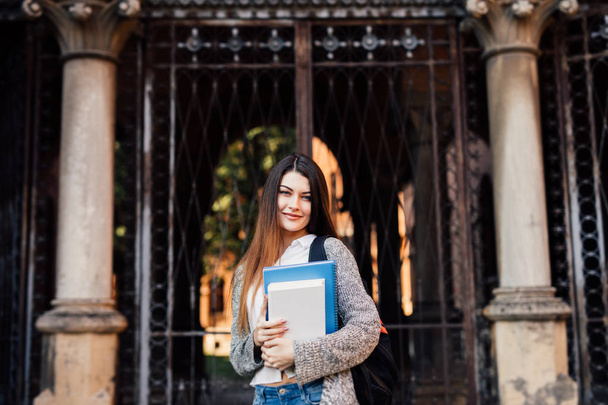 Studentessa all'aperto che tiene un quaderno e sorride vicino a Uni
 - Foto, immagini