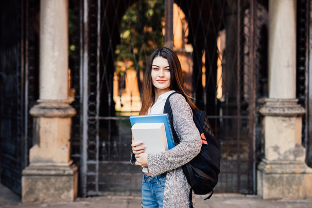 Porträt einer glücklichen Studentin, die Bücher in der Hand hält und in der Nähe der Universität in die Kamera blickt - Foto, Bild