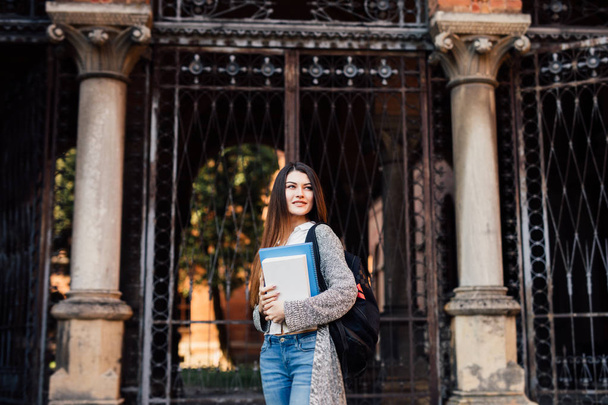 Улыбающаяся молодая девушка с рюкзаком, идущая на улицу возле кампуса
 - Фото, изображение