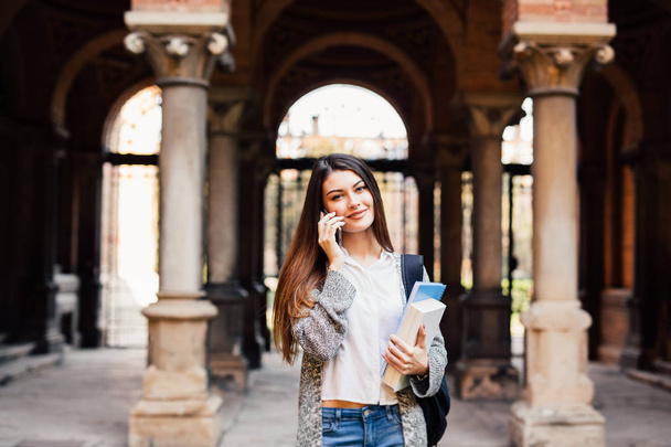 Nádherný šťastný student hospodářství notebooky hovoří telefon na koleji na vysoké škole - Fotografie, Obrázek