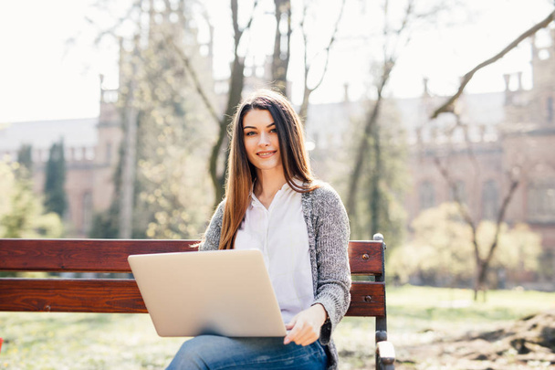 Student meisje met een laptop op een bankje in het park in de buurt van de campus - Foto, afbeelding