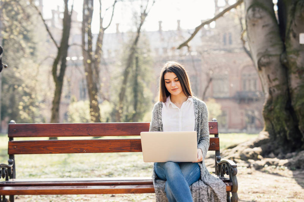 Jeune femme avec un ordinateur portable sur un banc de parc journée ensoleillée
 - Photo, image