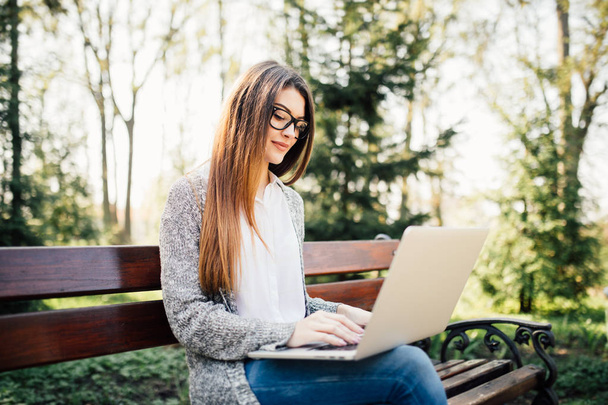 Chica joven en un banco con un ordenador portátil en el parque
 - Foto, Imagen