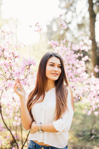 Açık çiçekli Manolya ağacı yakınındaki güzel bir genç kadının portresi. - Fotoğraf, Görsel