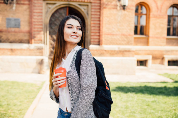 American university student smiling with coffee and book bag on campus - Photo, Image