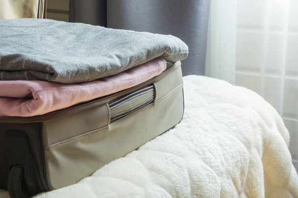 Open door and open suitcase with clothes on the bed. - Valokuva, kuva