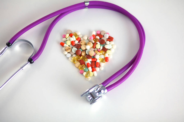 Lähikuva pillereitä levitetään taulukon stetoskooppi ja sydän makaa vieressä
 - Valokuva, kuva