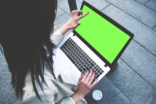 Подивіться сюди. Високий кут зору привабливої ділової жінки в розумному повсякденному носінні вказує на зелений екран ноутбука і друкує текст на клавіатурі, працюючи на ноутбуці на відкритому повітрі. Ноутбук ключа Chroma
. - Фото, зображення