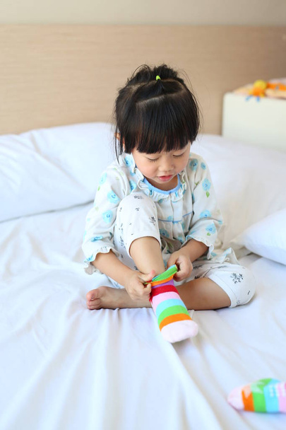 Adorable little girl trying to put a socks on the bed. - Foto, immagini