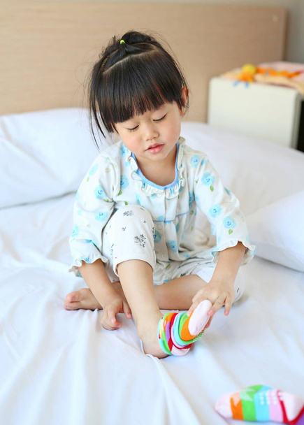 Adorable little girl trying to put a socks on the bed. - Foto, Imagem