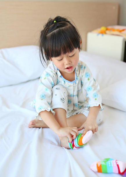 Adorable little girl trying to put a socks on the bed. - Zdjęcie, obraz
